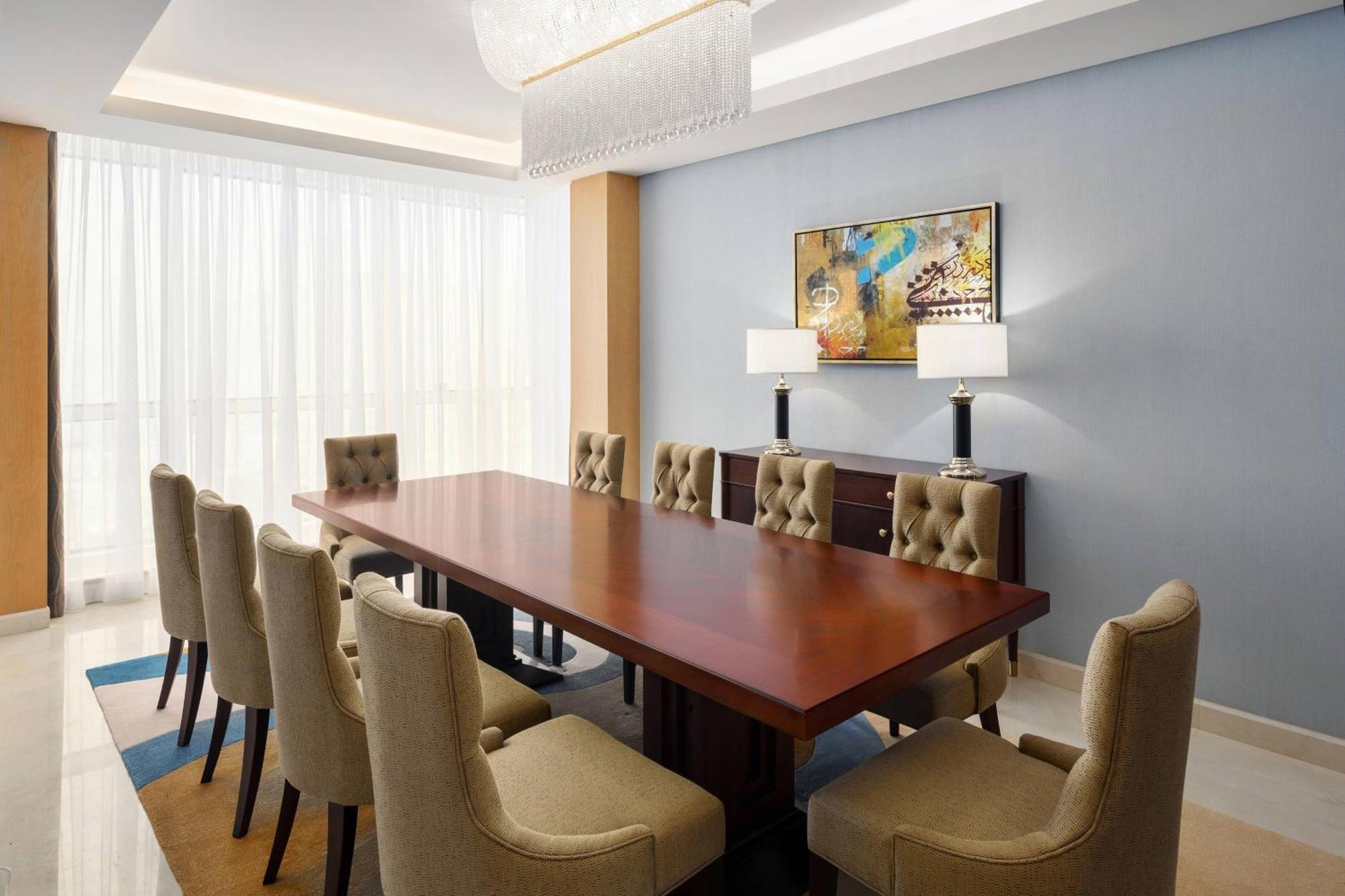 מכה Sheraton Makkah Jabal Al Kaaba Hotel מראה חיצוני תמונה The photo shows a spacious and elegantly designed conference room. It features a large wooden conference table surrounded by upholstered chairs. The chairs have a beige color and a tufted design. On one side of the room, there are two contemporary la