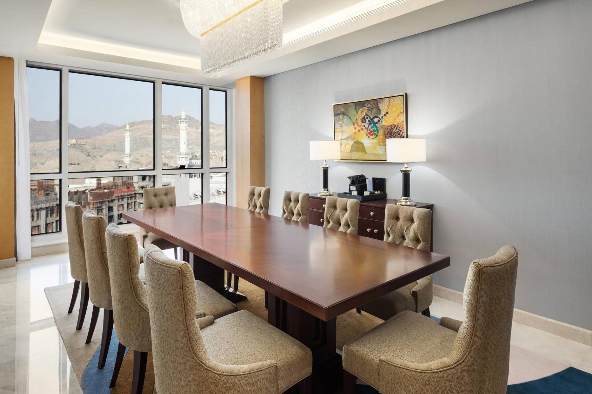 מכה Sheraton Makkah Jabal Al Kaaba Hotel מראה חיצוני תמונה The photo shows a modern conference room with a large wooden table surrounded by upholstered chairs. The room is well-lit, featuring large windows that offer a view of the outdoors, possibly with mountains in the background. On one wall, there is a p